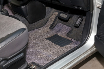 Dirty car floor mats of gray carpet with gas pedals and brakes in the workshop for the detailing...