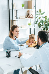 attentive mother with son looking at doctor in hospital