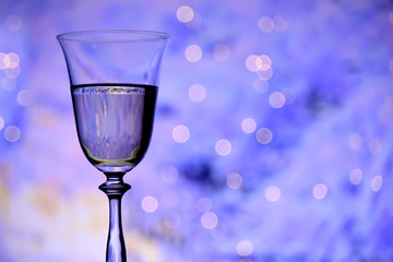 Glass with champagne sparkling wine on a festive blue background with lights and bokeh. The atmosphere of celebration and happiness.