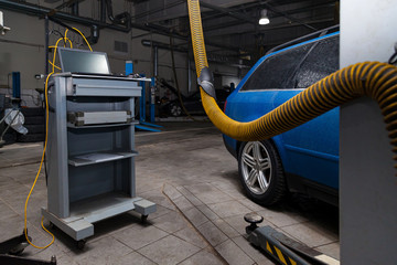 Car service interior with a computer for reading electronic errors during the diagnosis of a blue car on a lift with a yellow hood in a vehicle repair workshop. Auto service industry.