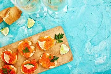 Salmon red caviar in bowl and Sandwiches with on wooden cutting board, glass with champagne on blue background copy space. Top view.