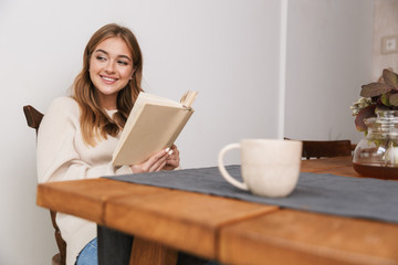 Image of smiling caucasian woman reading book and drinking tea