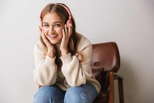 Image of pleased young woman smiling and using headphones while sitting