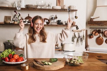 Image of smiling woman using headphones and dancing while cooking