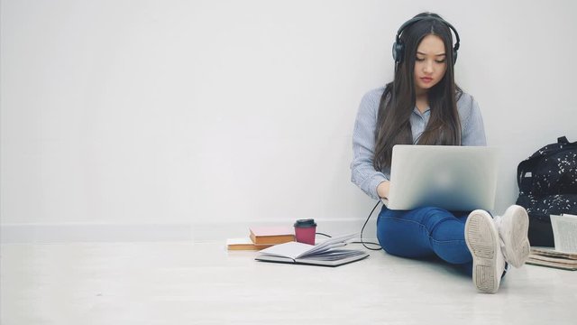 A schoolgirl sits on the floor on a white background. With a laptop. Holds a notepad with a note back to school.