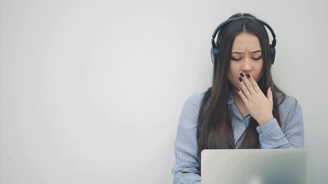 Lovely but tired asian girl with long hair sitting with laptop on her knees, yawning, massaging temples, having some difficulties.