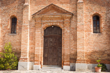 Fototapeta na wymiar Wooden door of an exposed brick church. Ozzano Monferrato