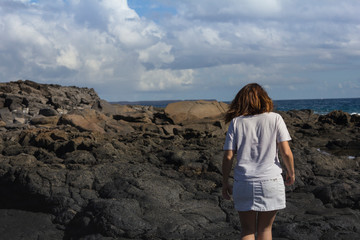 Women with summer clothes on volcanic rocks and blue ocean