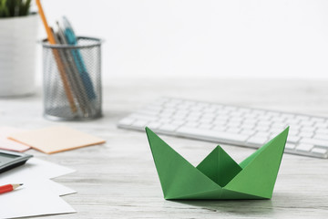 Top view office workspace with green paper ship
