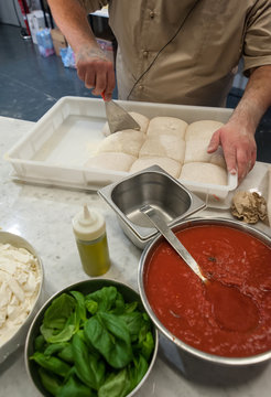 Preparing Pizza dought on a marble top. Tomato sauce, mozzarella and other ingredients in the foregound.