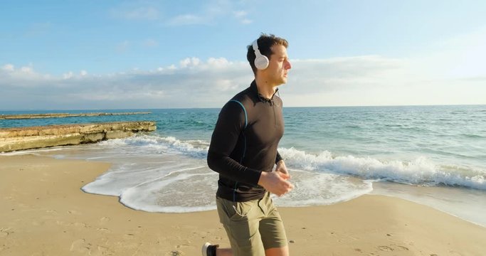 Fit male runner training on the summer beach and listen to music against beautidul sky and sea , UHD 4K