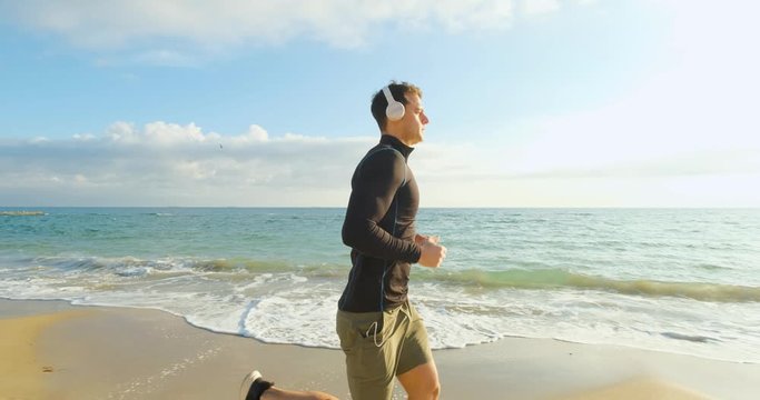 Fit male runner training on the summer beach and listen to music against beautidul sky and sea , UHD 4K