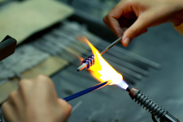 Artist of glass at work. Hand made glass beads in the fire out of red hot glowing glass for pandora bracelets,focus glass bead around blurry
