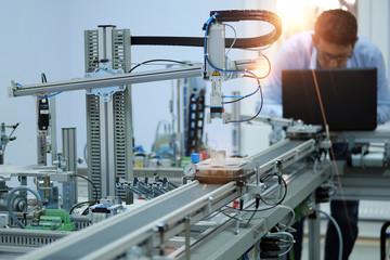 Industry 4.0 workshop in an automation education center. Engineer is programming PLC. Focus on Gripper which picks up the product from an automated car and programming engineer at the background.