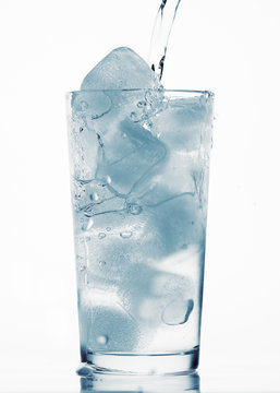 pouring water in a glass full of ice cubes, white background, blue toned object