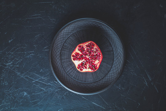 Fresh juicy pomegranate - whole and cut on a black vintage background, top view, horizontal, with copy space.