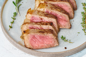 Keto ketogenic diet beef steak, striploin on gray plate on white background. Paleo food recipe with chopped piece of meat and seasoning. Close up, side view