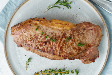 Keto ketogenic diet beef steak, striploin on gray plate on white background. Paleo food recipe with whole big piece of meat and seasoning. Macro, close up, top view
