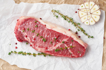 Big whole piece of raw beef meat, striploin on white parchment paper on craft background, zero waste packing. Seasoning steak with salt
