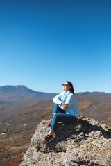 Naklejka na ściany i meble A girl sits on a rock in the mountains and enjoying view of nature. Nature background. Journey. A trip to the mountains.