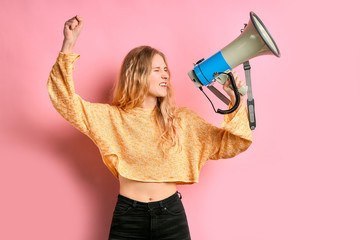 portrait of young feminist girl holding loudspeaker in hands promoting feminism to society, stand isolated over pink background