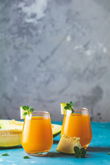 Yellow orange cocktail with melon and mint in glass on blue concrete background, close up. Summer drinks and alcoholic cocktails