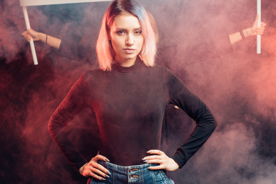 portrait of young caucasian girl feminist isolated in smoky space, wearing black blouse, look at camera