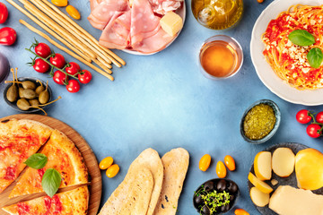 Italian food background. Pizza, pasta, cheese, hams, wine, olives, pesto, capers, shot from the top, forming a frame for copy space, a flat lay composition