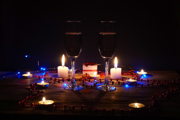 Champagne glasses on the table among the candles, hearts, beads, garlands and a gift in the center. the concept of a romantic dinner, offer hands and hearts