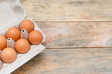Brown chicken eggs in cardboard packaging on wooden background with copy space, view top