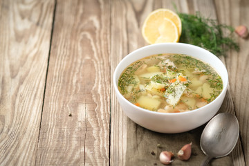 Fresh homemade fish soup with vegetables in bowl on rustic wooden background with copy space.