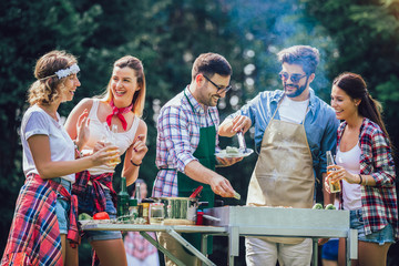 Young friends having fun grilling meat enjoying barbecue party.