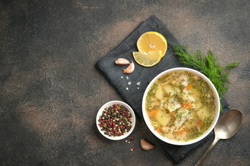 Fresh homemade fish soup with vegetables in bowl on black background, top view