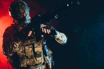 Fototapeta premium warrior military man wearing green uniform stand with gun rifle isolated over smoky background with ultra-violet rays, in search of enemy