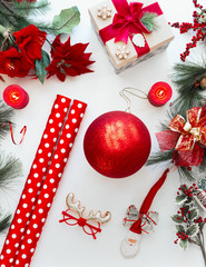Red Christmas decoration and wrapping paper on white desk with fir branches and Christmas flowers....
