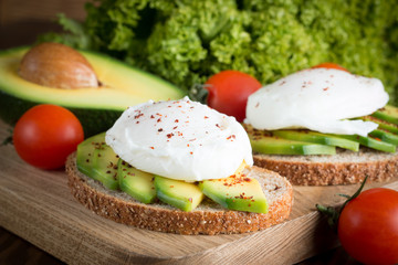 Avocado toast, cherry tomato and poached eggs on wooden background. Breakfast with vegetarian food, healthy diet concept.