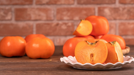 Fresh beautiful sliced sweet persimmon kaki on dark wooden table with red brick wall background,...
