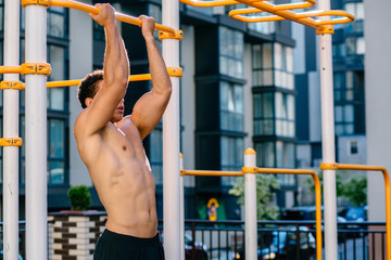 Fototapeta na wymiar Sporty man enjoying music during workout outdoors, doing chin-ups on horizontal bars