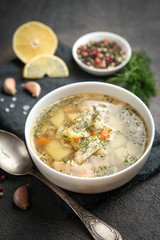 Fresh homemade fish soup with vegetables in bowl on black background.