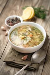 Fresh homemade fish soup with vegetables in bowl on rustic wooden background.