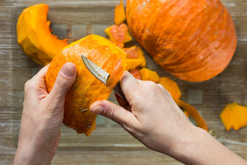 Peeling off pumpkin with ordinary knife by woman hand on the wooden background