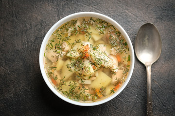 Fresh homemade fish soup with vegetables in bowl on black background, top view with copy space.
