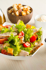 Fresh Caesar salad with delicious chicken breast, ruccola, spinach, cabbage, arugula, egg, parmesan and cherry tomato on wooden background. Oil, salt and pepper. Healthy and diet food concept.