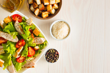 Fresh Caesar salad with delicious chicken breast, ruccola, spinach, cabbage, arugula, egg, parmesan and cherry tomato on wooden background. Oil, salt and pepper. Healthy and diet food concept.