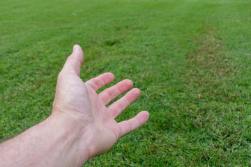 Conceptual open hand reaching out on green grass. Openness, giving, assistance and helping concepts.