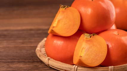 Fresh beautiful sliced sweet persimmon kaki on dark wooden table with red brick wall background, Chinese lunar new year fruit design concept, close up.