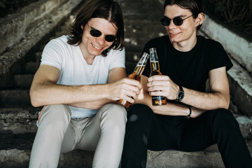 Two Stylish Twins Brothers Having Fun Drinking Beer on the Stairs