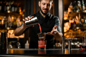 Bartender pours red liquor from shaker through sieve