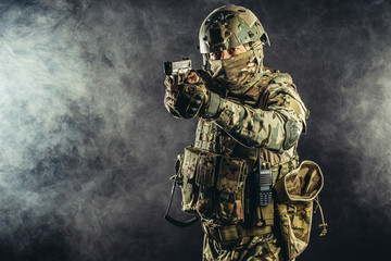 fearless brave strong man with gun isolated in black foggy space, in readiness to shoot at enemy, wearing military uniform
