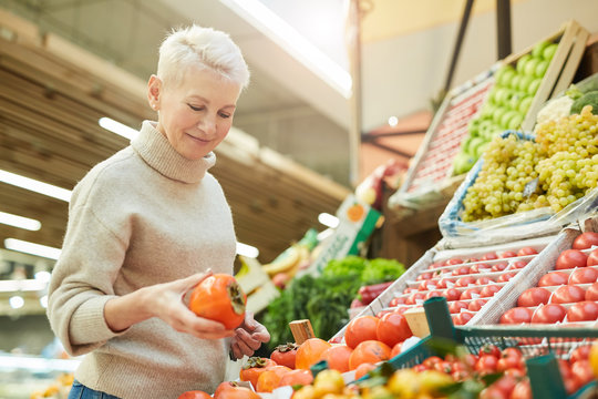 Waist up portrait of beautiful adult woman choosing fresh vegetables while grocery shopping at farmers market, copy space